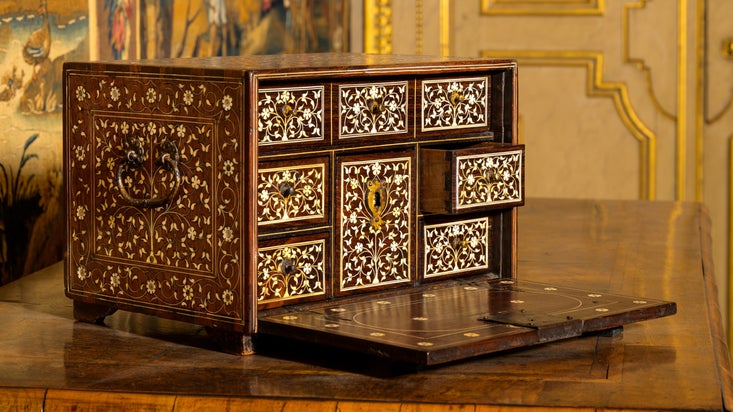 Ivory inlay miniature cabinet on a table in the North Drawing Room with wall hangings and a door in the background at Ham House and Garden, London